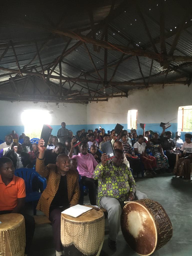 Believers in a refugee camp church waving their new Bibles